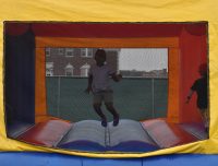 A smiling child in a yellow, blue, and red bounce house jumping happily