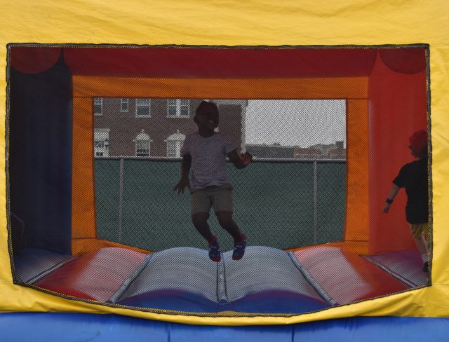 A smiling child in a yellow, blue, and red bounce house jumping happily