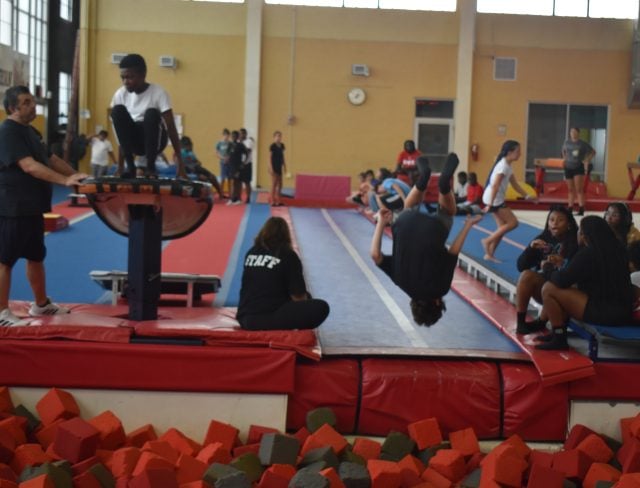 Two campers jumping into the foam pit in Gymnastics, one is mid-air, tumbling and the other is poised ready to jump