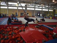 a girl with blonde hair swings on a rope over a foam pit, smiling while enjoying the aviator camp facilities