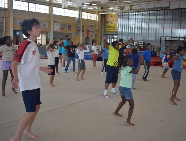 Young gymnasts stretching for gymnastics warmups before participating in camp activities like gymnastics