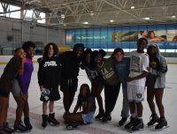 A group of youth wearing ice skates and smiling posing on the ice