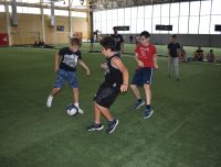 Three young campers playing soccer on the turf fields, wearing t-shirts and shorts while dribbling a ball together